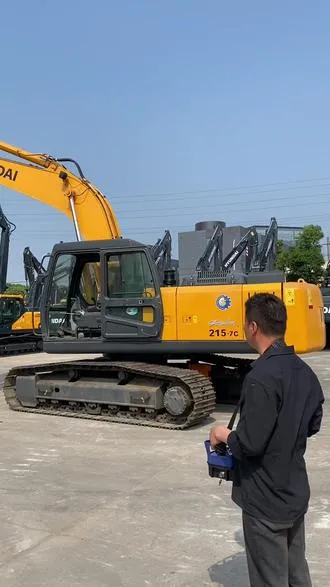 Worker operating an excavator remotely using a wireless remote control at a construction site.